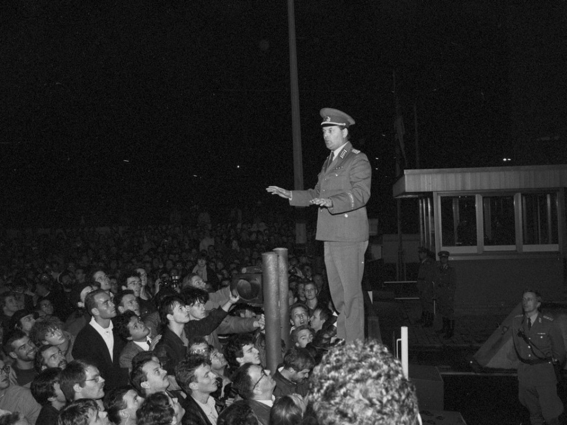 Schrz-weiß Foto eines Grenzsoldaten bei Nacht, stehend auf einem Tor, davor eine Menschenmenge