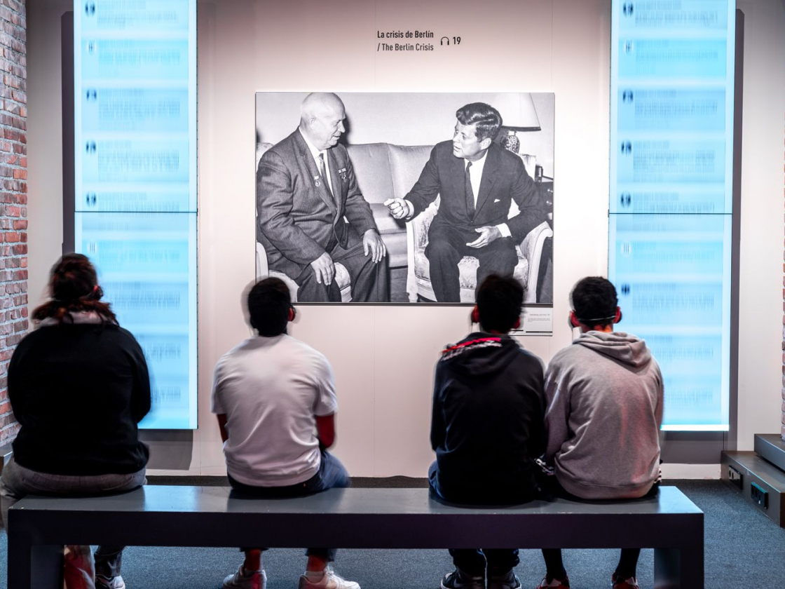 Besucher sitzen in einer Ausstellung auf einer Bank vor einem Bild