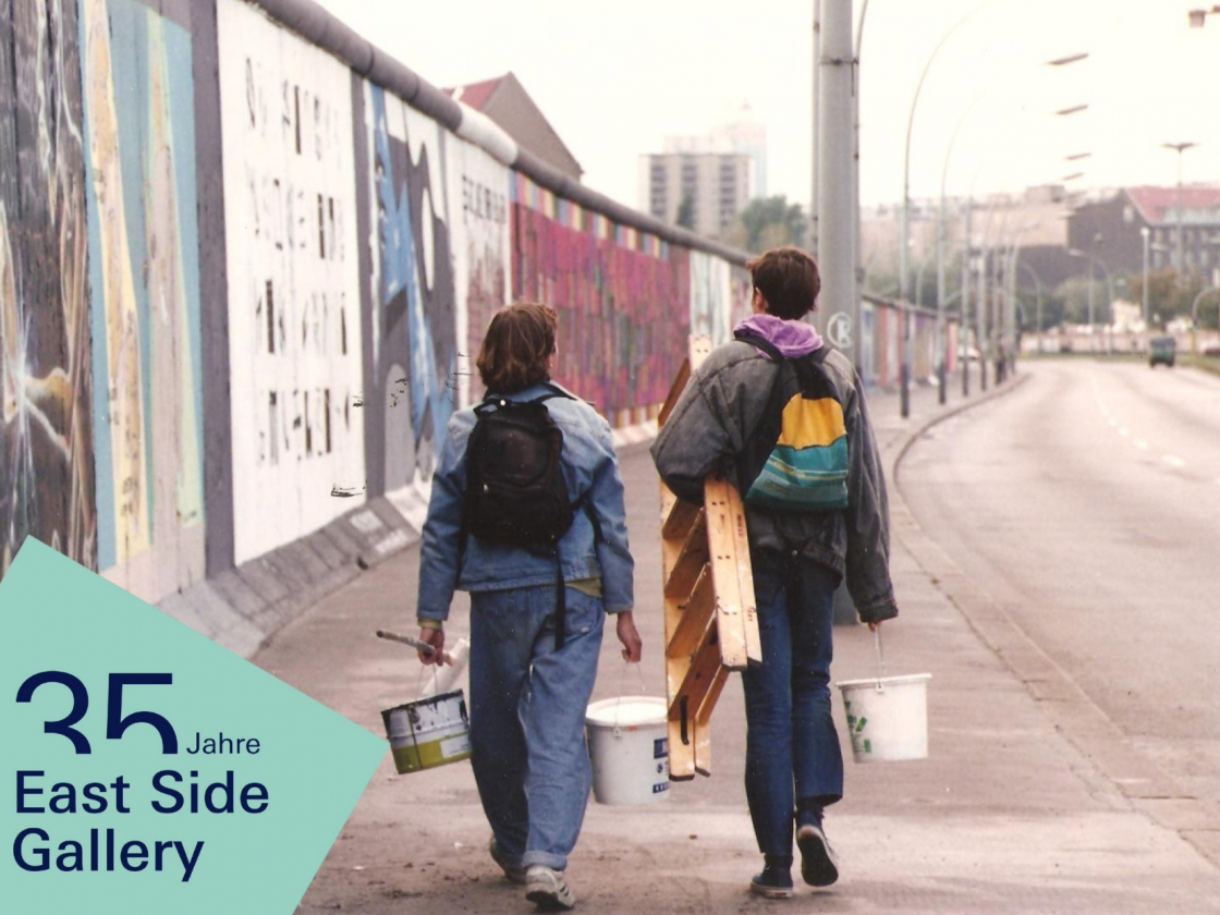 Personen mit Malwerkzeugen laufen entlang der East Side Gallery