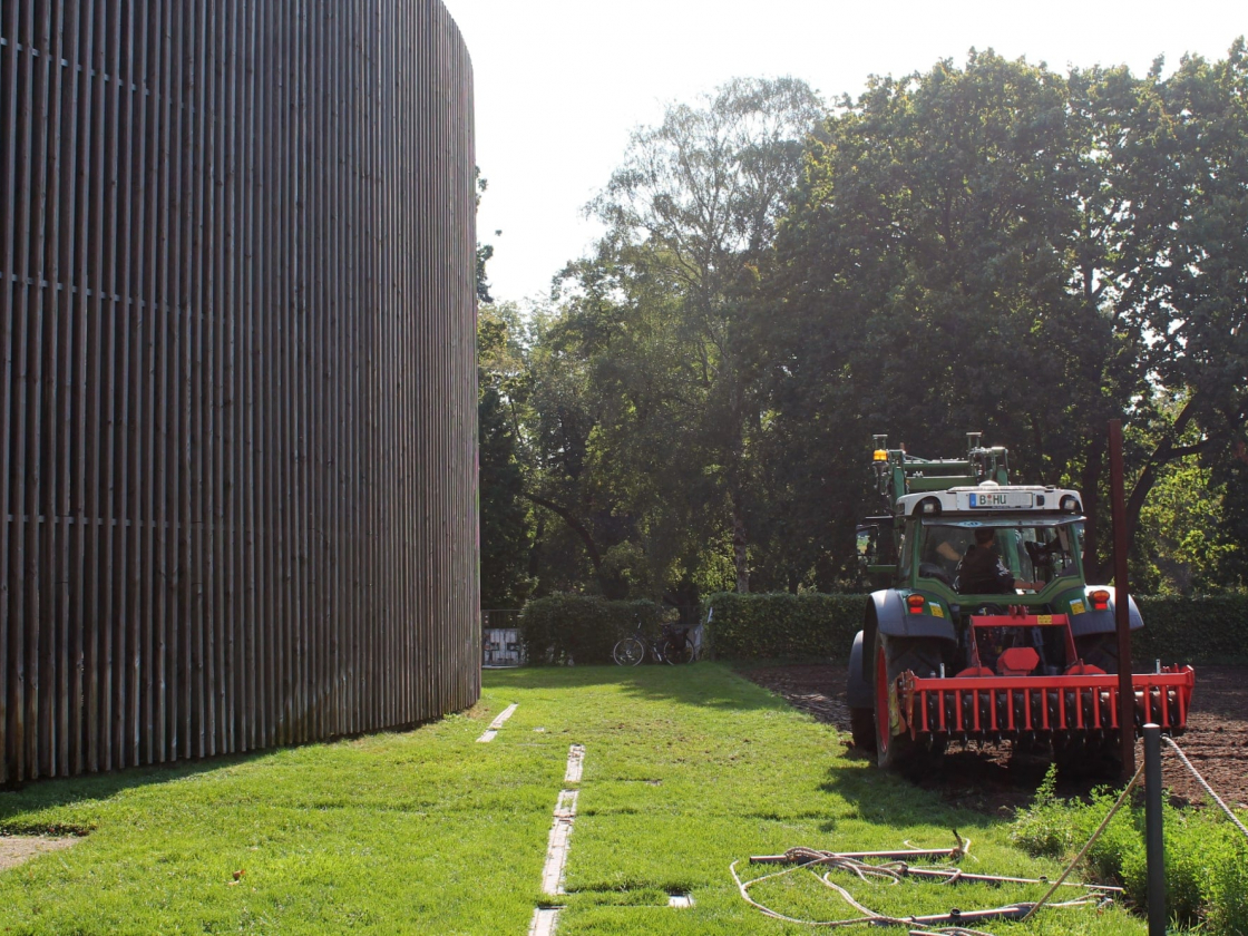 Ein Traktor fährt über ein Feld. Auf der linken Seite ist die Kapelle der Versöhnung zu sehen. 