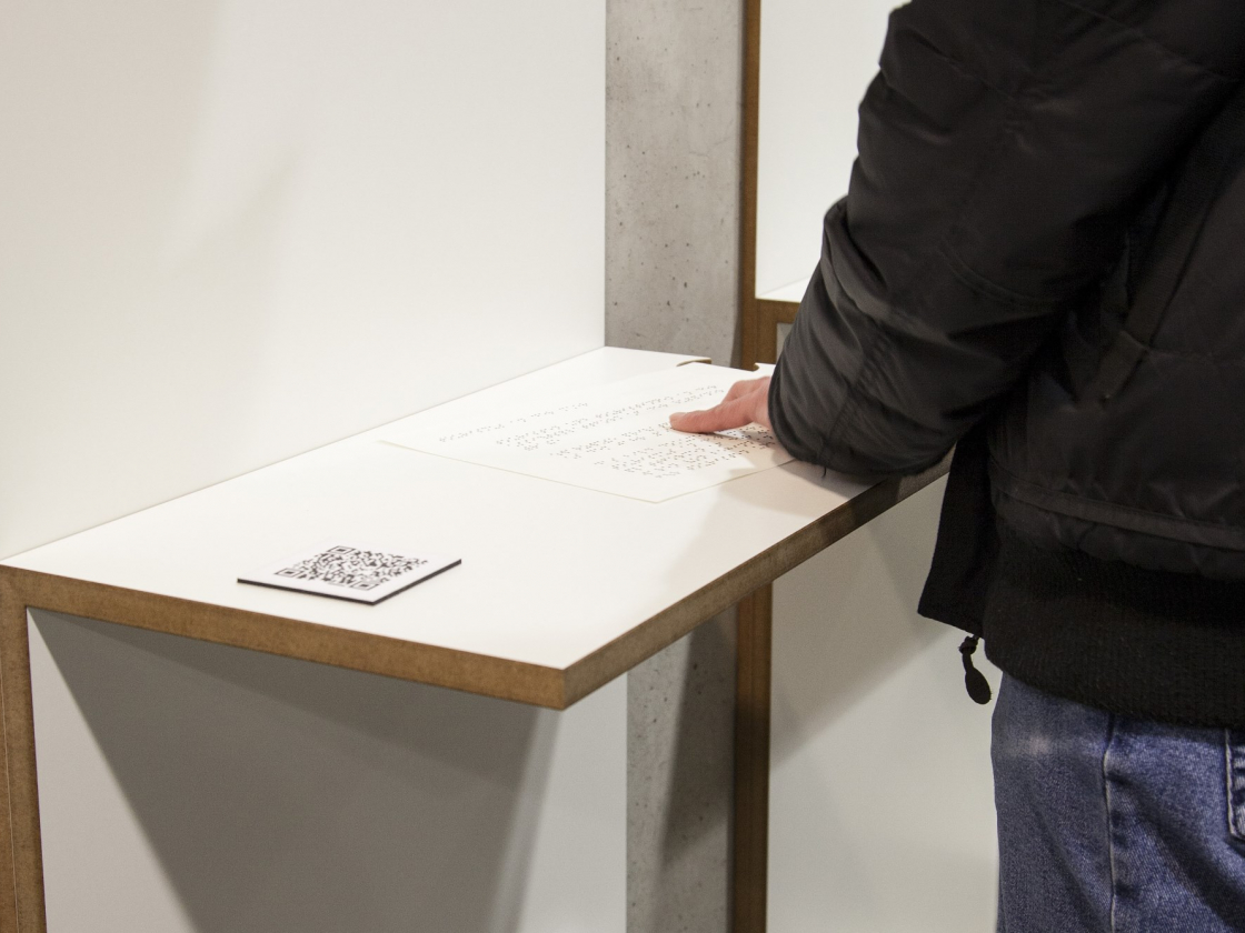 Person ertastet Brailleschrift am Ausstellungsmodul