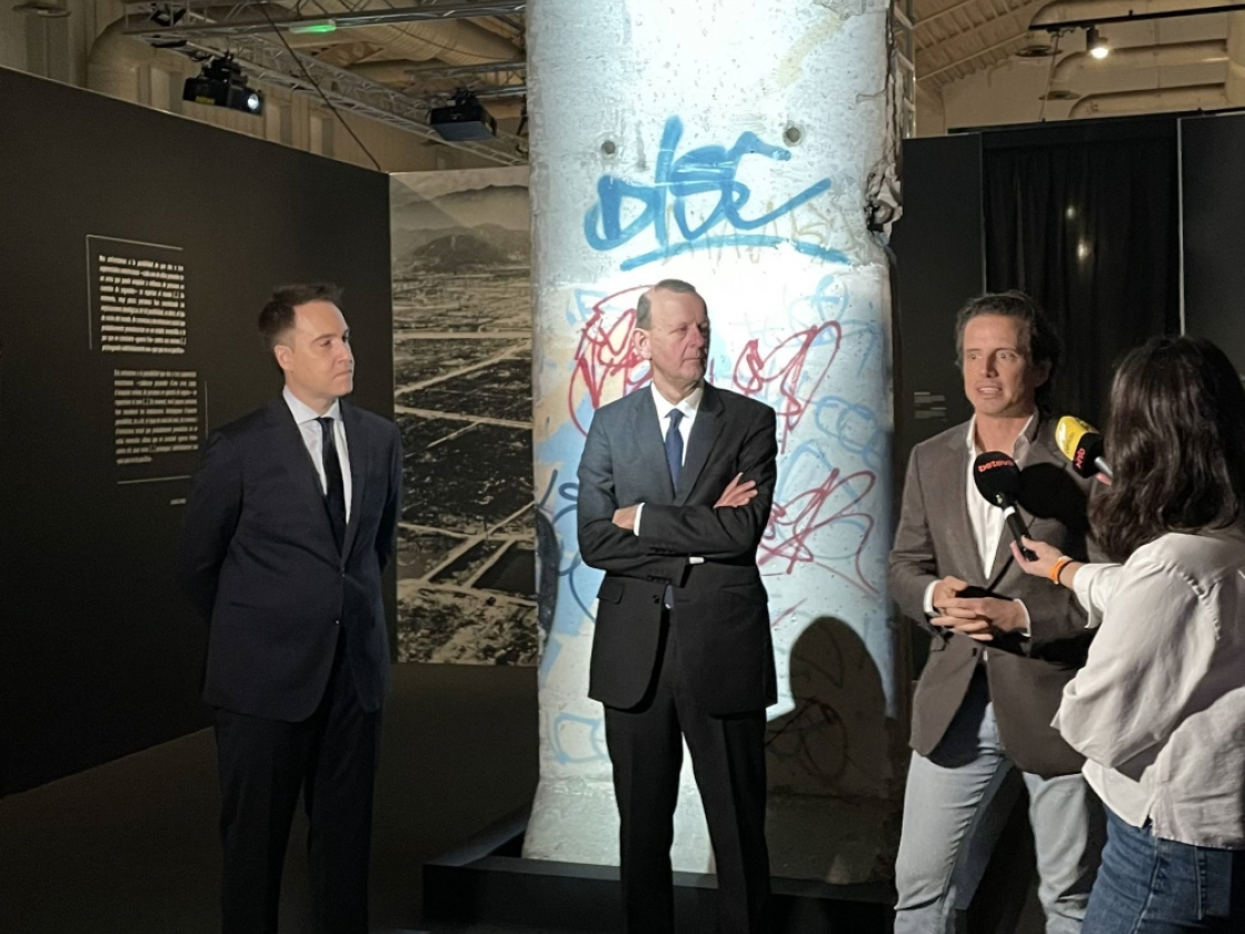 Drei Personen und eine Journalistin stehen vor einem Mauerstück in der Ausstellung