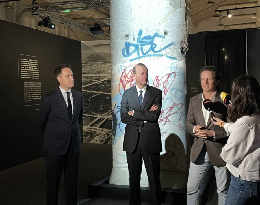 Drei Personen und eine Journalistin stehen vor einem Mauerstück in der Ausstellung