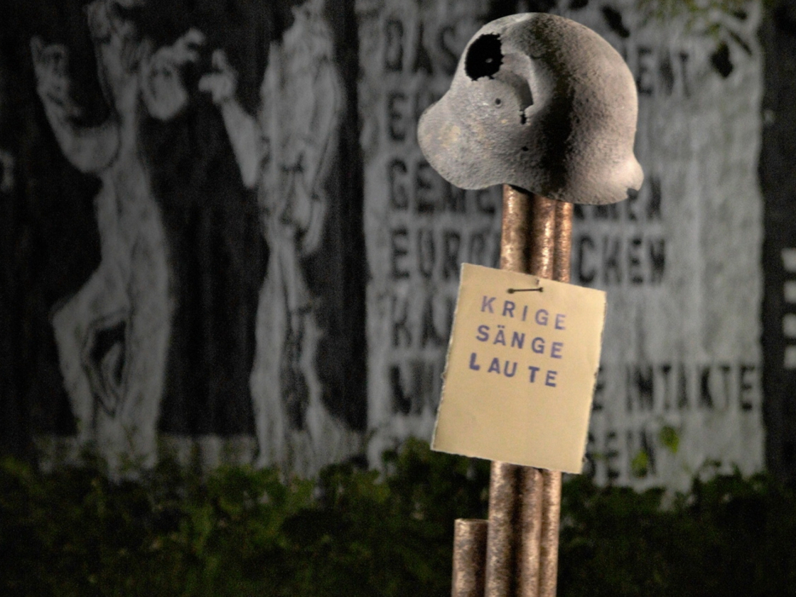 Rostiger Wehrmachtshelm vor bemalten Mauerteilen im Parlament der Bäume