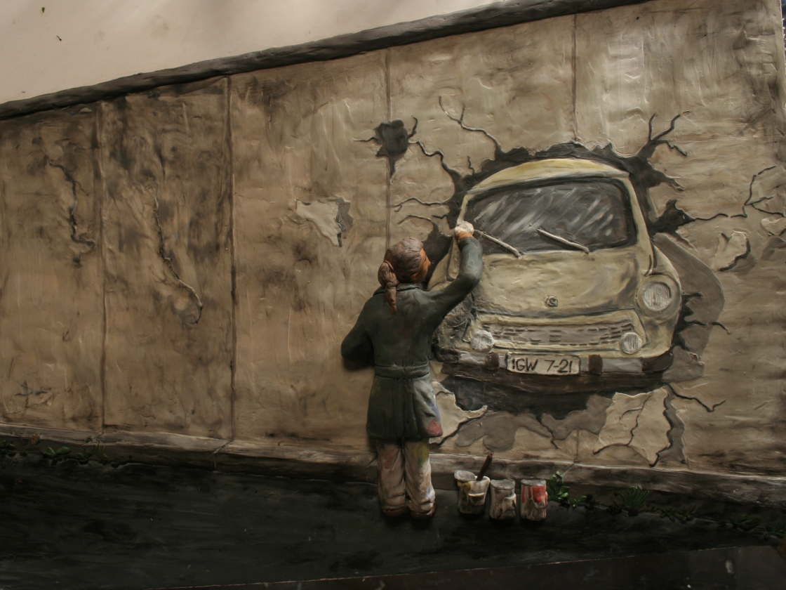 Still von einem Animationsfilm wo eine Person zu sehen ist, die auf die Mauer ein Graffiti von einem Trabi malt.